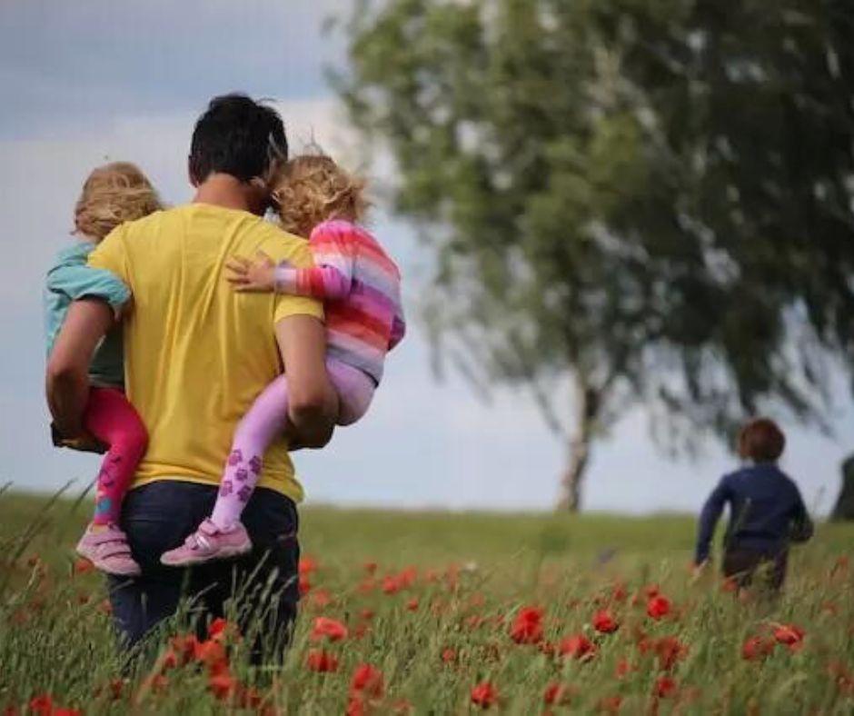 father walking with kids to tree outdoors through meadow